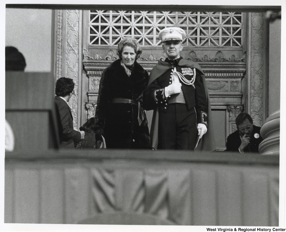 ["Blanchette Rockefeller being escorted to the dais by an officer shortly before the inauguration of her son, Governor Jay Rockefeller."]%